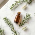 Çay ağacı yağı şişesi ve Melaleuca alternifolia yaprakları — beyaz mermer üzeri