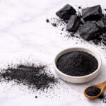 Aktif karbon parçaları ve ince siyah toz — beyaz mermer üzeri hindistancevizi kabuğu